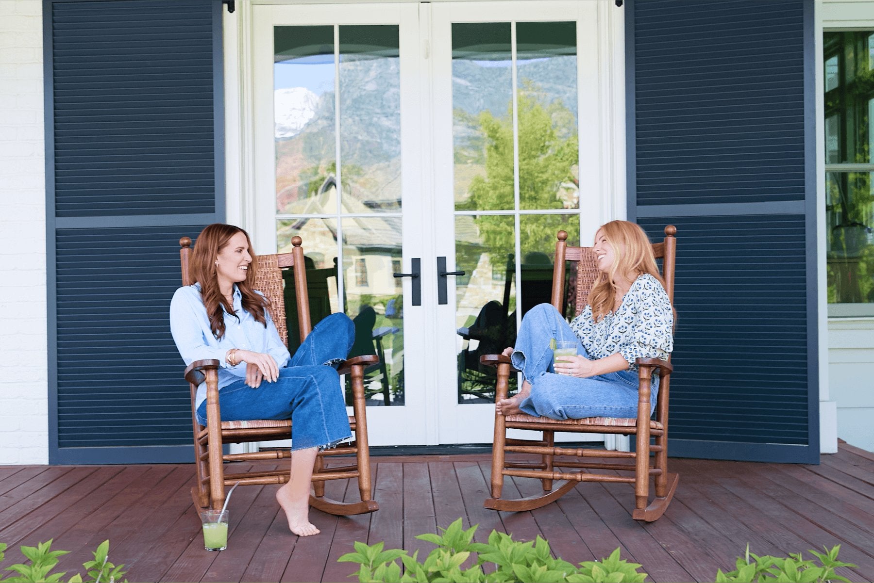 The two co-founders sitting and talking in rocking chairs on a covered porch, each with a tall green drink beside them.